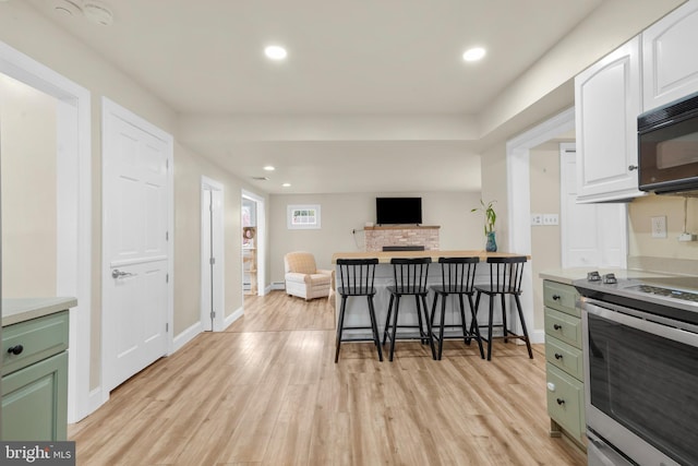 kitchen featuring light wood-type flooring, electric stove, black microwave, and open floor plan