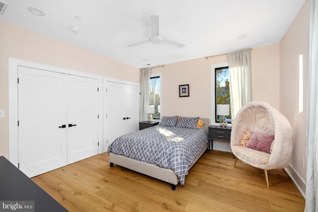 bedroom with light wood-style floors, two closets, visible vents, and a ceiling fan