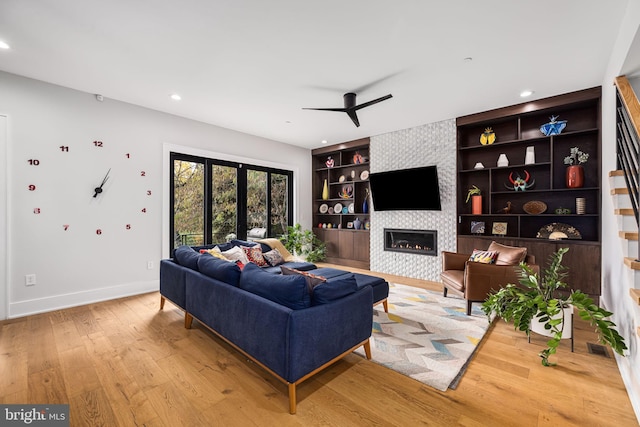 living room with light wood finished floors, baseboards, a tiled fireplace, built in features, and ceiling fan