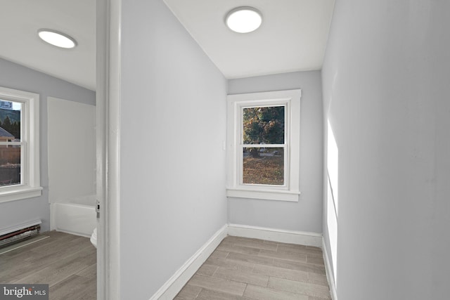 hallway featuring a baseboard heating unit, light wood-style floors, and baseboards