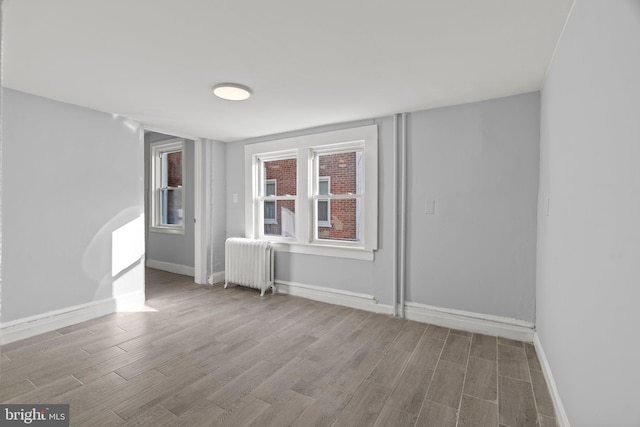 unfurnished room featuring radiator, baseboards, and wood finished floors