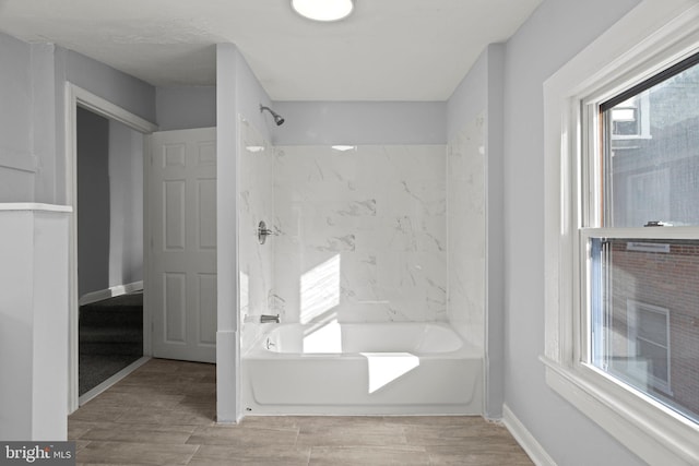full bathroom featuring washtub / shower combination, wood finished floors, and baseboards