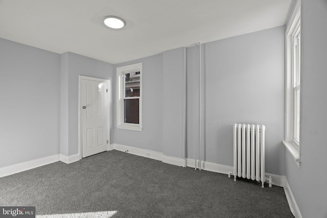 unfurnished room featuring radiator heating unit, baseboards, and dark carpet