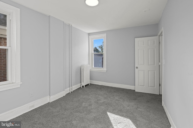 unfurnished bedroom with radiator, dark colored carpet, and baseboards
