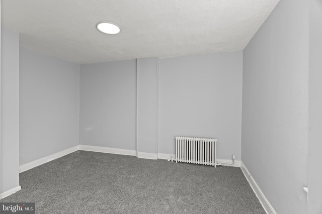 empty room featuring dark carpet, radiator, baseboards, and a textured ceiling