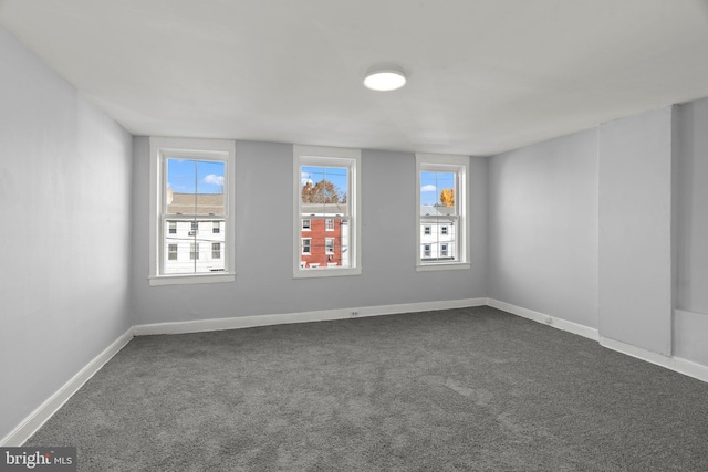 unfurnished room with baseboards and dark colored carpet