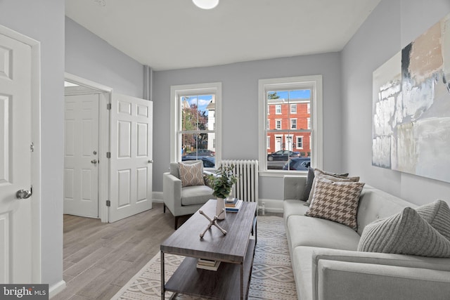 living room featuring radiator heating unit, baseboards, and light wood finished floors