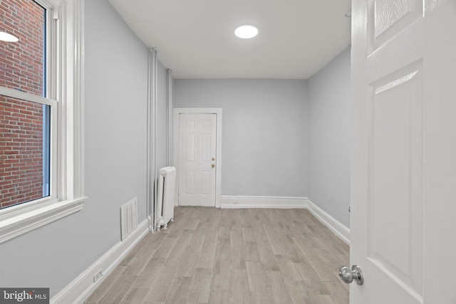 spare room featuring radiator, baseboards, wood finished floors, and visible vents