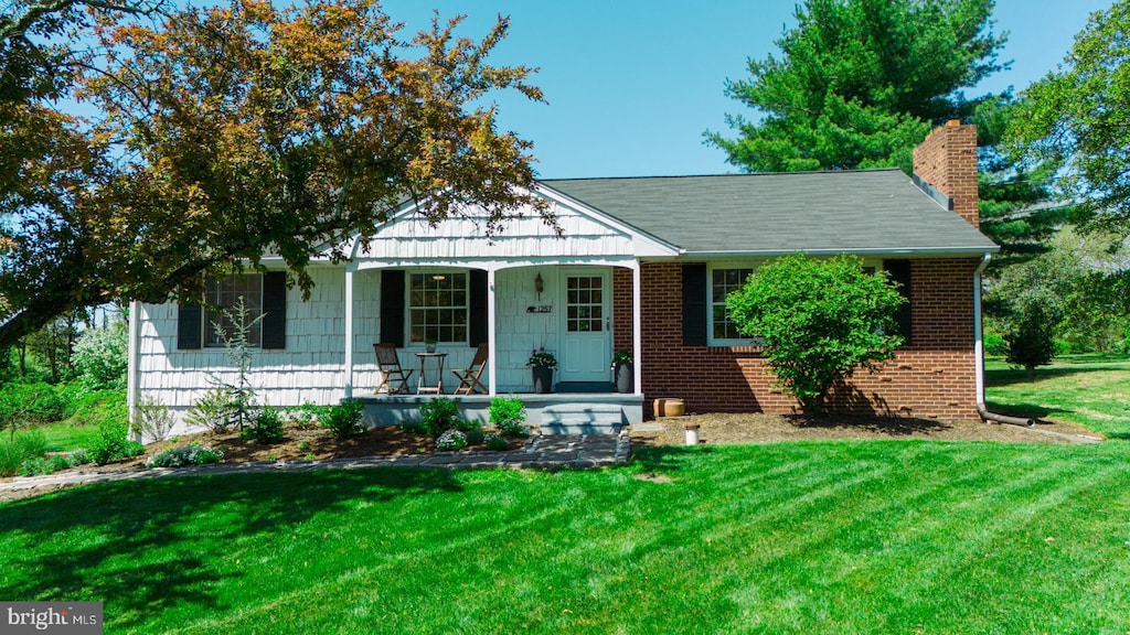 ranch-style home featuring covered porch, a chimney, a front lawn, and brick siding