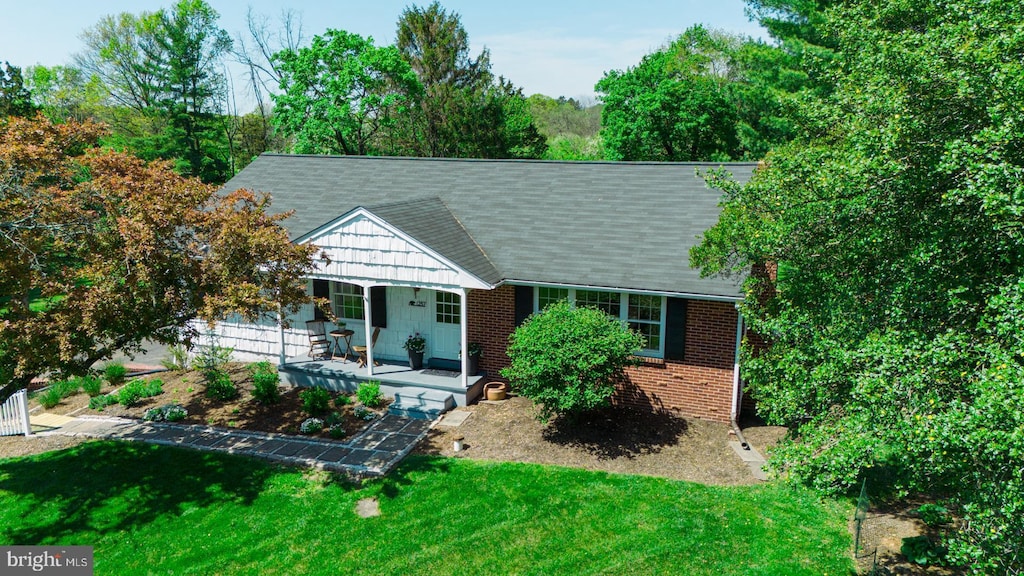 ranch-style home with brick siding, roof with shingles, covered porch, and a front yard