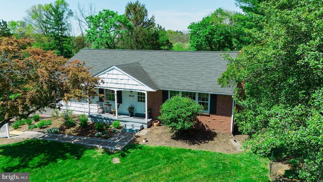 ranch-style home with brick siding, roof with shingles, covered porch, and a front yard