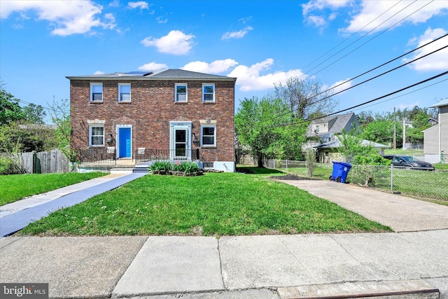 view of front of property featuring brick siding, a front lawn, roof mounted solar panels, and fence