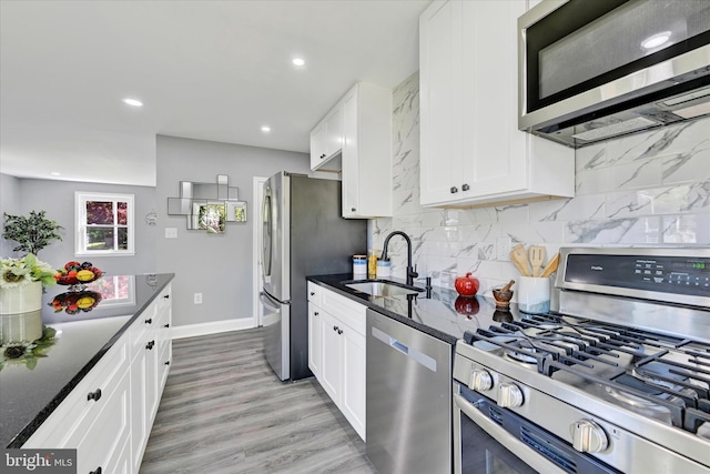 kitchen with white cabinetry, a sink, light wood-style flooring, backsplash, and stainless steel appliances