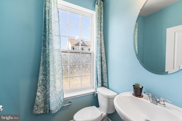 half bathroom featuring a sink, toilet, and a healthy amount of sunlight