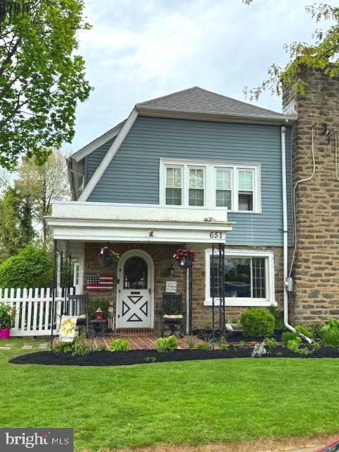 view of front of house with fence, a porch, a front lawn, and stone siding