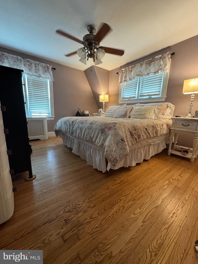 bedroom with radiator heating unit, wood finished floors, a ceiling fan, and baseboards