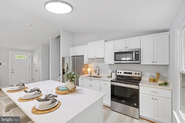 kitchen featuring stainless steel appliances, a sink, vaulted ceiling, white cabinets, and light countertops