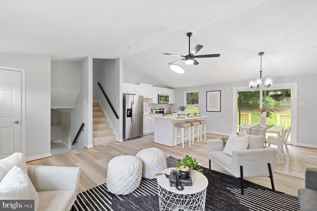 living room featuring light wood-style flooring, ceiling fan, stairs, vaulted ceiling, and a chandelier