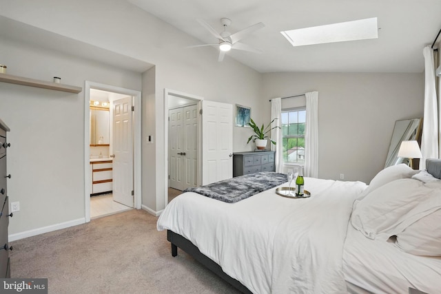 bedroom with ensuite bath, light colored carpet, ceiling fan, baseboards, and lofted ceiling with skylight