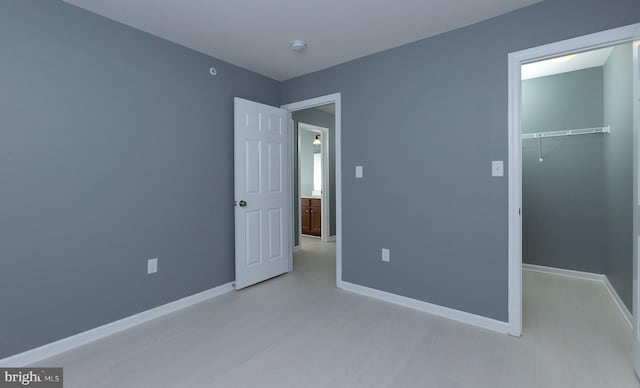 unfurnished bedroom with light wood-style flooring, baseboards, a closet, and a walk in closet