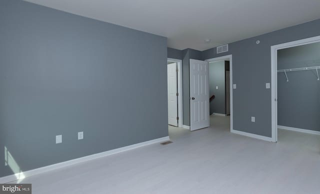 unfurnished bedroom featuring a closet, a spacious closet, light wood finished floors, baseboards, and visible vents