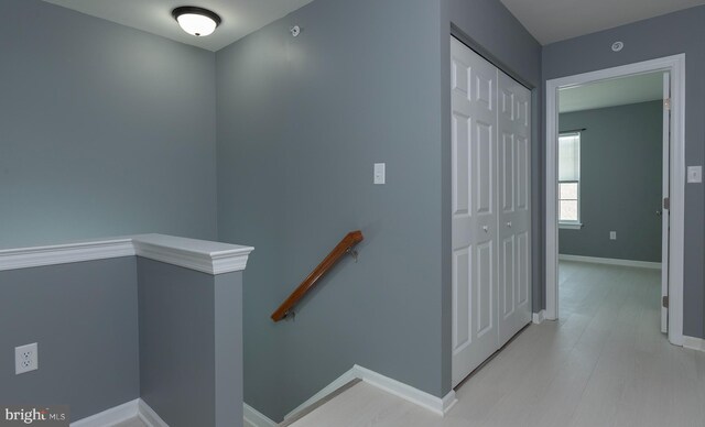 hall with wood finished floors, baseboards, and an upstairs landing