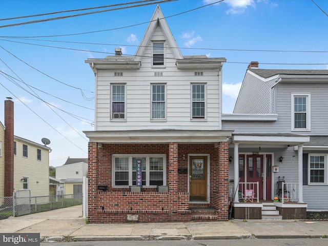 view of front of home with brick siding, fence, and covered porch