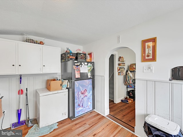 laundry room with arched walkways, a textured ceiling, and light wood finished floors