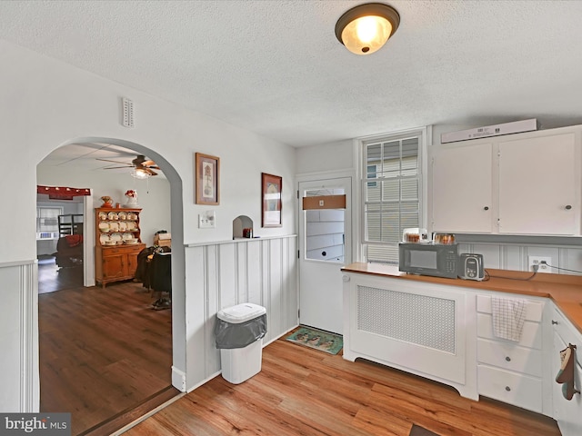 kitchen with black microwave, arched walkways, a textured ceiling, light wood-style flooring, and white cabinetry