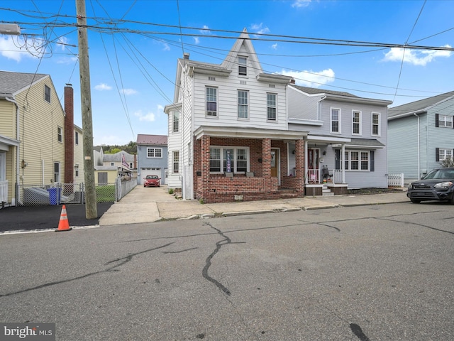 view of front of home with covered porch, brick siding, and fence