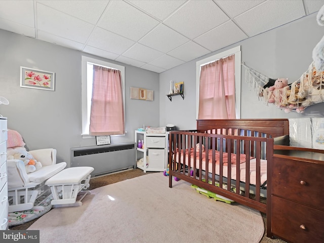 bedroom featuring radiator, a paneled ceiling, carpet, and a nursery area