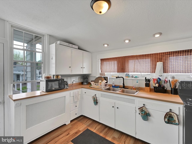 kitchen with a sink, a textured ceiling, black microwave, and light countertops