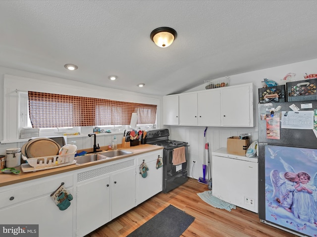 kitchen featuring freestanding refrigerator, black electric range oven, white cabinets, a sink, and vaulted ceiling