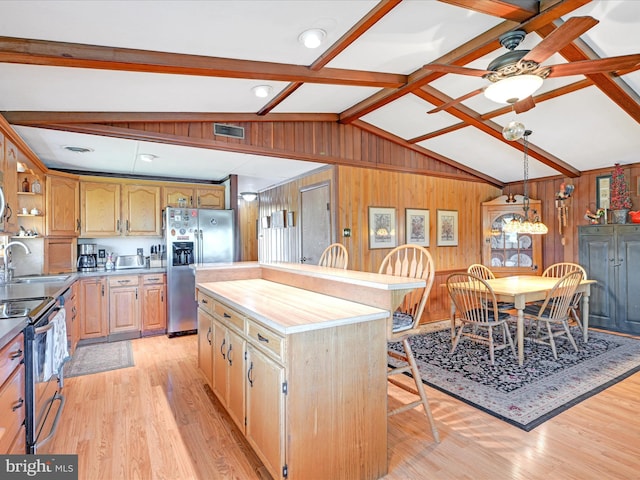 kitchen featuring appliances with stainless steel finishes, wood walls, a sink, light wood-style floors, and vaulted ceiling with beams