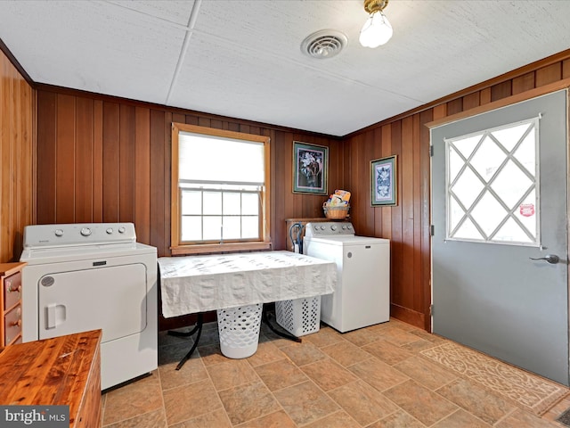 laundry room featuring laundry area, wood walls, visible vents, washer and dryer, and stone finish flooring