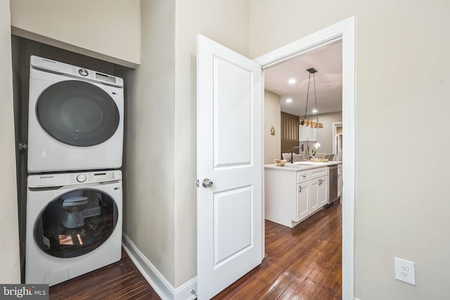 clothes washing area featuring a sink, laundry area, baseboards, stacked washer and clothes dryer, and dark wood-type flooring
