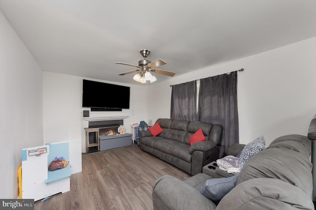 living room featuring ceiling fan, a lit fireplace, and wood finished floors
