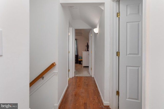 hallway featuring vaulted ceiling, wood finished floors, baseboards, and an upstairs landing