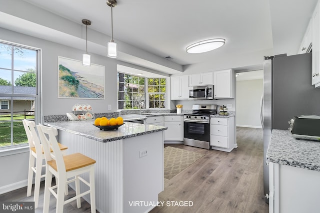 kitchen with a sink, stainless steel appliances, a healthy amount of sunlight, a peninsula, and white cabinetry