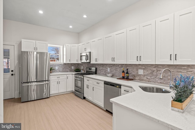 kitchen featuring light stone counters, a sink, decorative backsplash, white cabinets, and appliances with stainless steel finishes