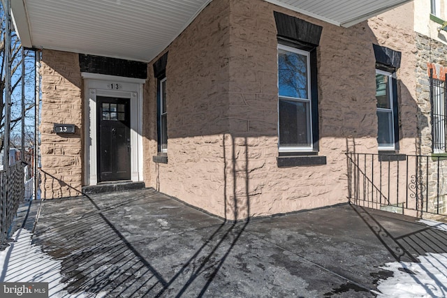 property entrance with covered porch, stone siding, and stucco siding