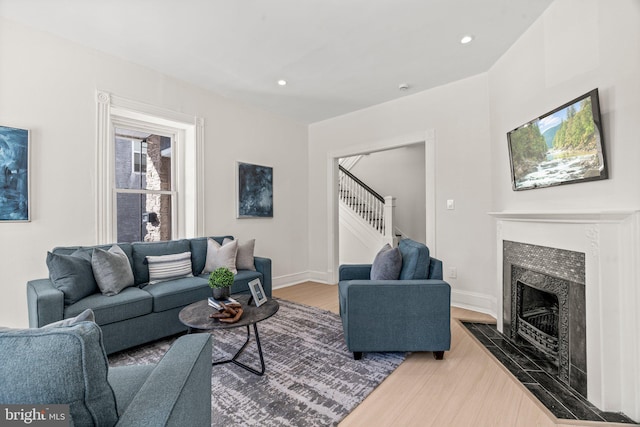 living room with recessed lighting, a high end fireplace, wood finished floors, baseboards, and stairs