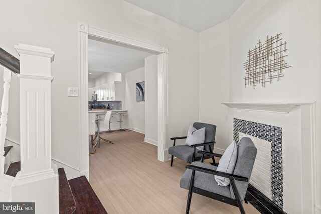 sitting room featuring light wood-type flooring, baseboards, a fireplace, and stairs