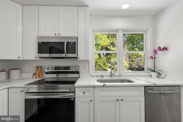 kitchen with light stone counters, appliances with stainless steel finishes, white cabinetry, and a sink