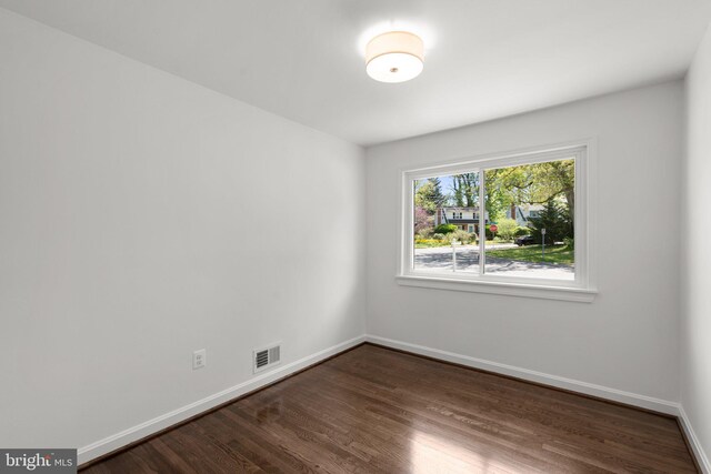 empty room with dark wood-type flooring, visible vents, and baseboards