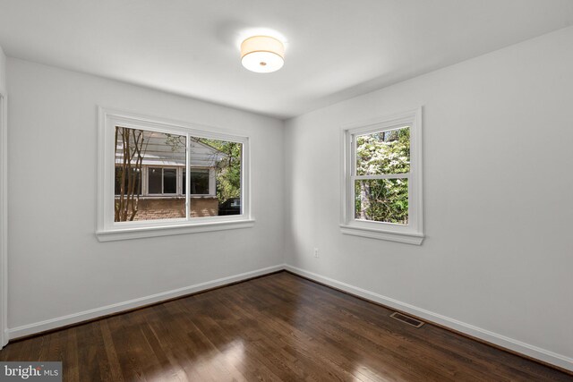 spare room featuring dark wood-style flooring, visible vents, and baseboards