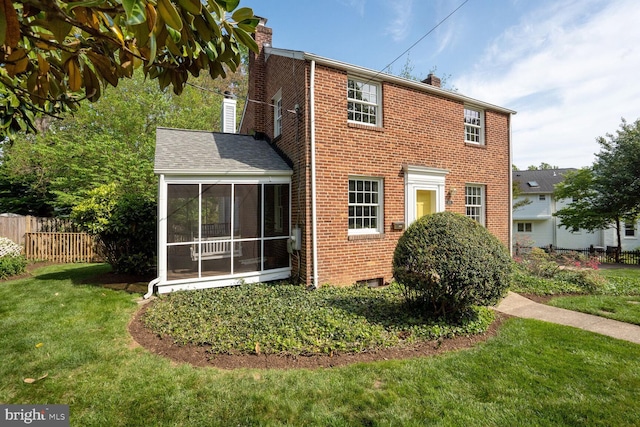 rear view of house featuring fence, brick siding, a yard, a chimney, and a sunroom