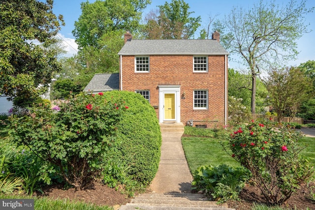 view of front of house featuring roof with shingles, brick siding, and a chimney