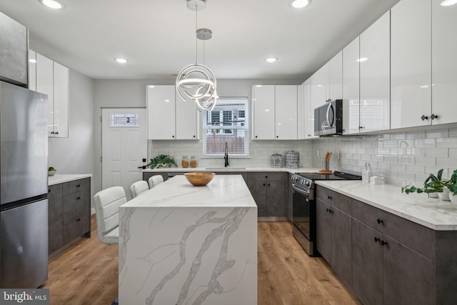 kitchen with a sink, modern cabinets, light wood-type flooring, appliances with stainless steel finishes, and white cabinetry