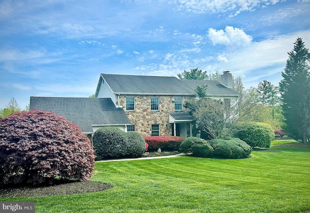 colonial home with a chimney, a front lawn, and stone siding